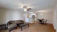 This single-floor residence offers a seamlessly connected open-concept layout that integrates the living, dining, and kitchen areas into one cohesive, functional space. Light hardwood flooring runs throughout, lending warmth and continuity to the interior.

The living area is comfortably proportioned and anchored by a ceiling fan with integrated lighting, providing both comfort and illumination. The space flows naturally into a casual dining area, distinguished by a stylish pendant light overhead and a chair-rail accent along the wall, adding a touch of architectural detail.

The kitchen is positioned at the heart of the home, defined by a peninsula counter that creates a natural boundary while maintaining the open feel. White cabinetry lines the upper walls, complemented by stainless steel appliances including a microwave and range, along with a refrigerator. Recessed overhead lighting brightens the workspace.

The overall ambiance is clean, bright, and inviting, with neutral white walls that enhance the sense of openness and allow natural light to circulate freely. The layout is practical and well-suited for everyday living, offering clear sightlines across all three connected areas from any vantage point in the room.