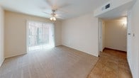 This single-story space offers a straightforward, functional layout designed for comfortable everyday living. The living area serves as the central gathering space, finished with plush wall-to-wall carpeting and anchored by a ceiling fan with integrated lighting. A large sliding glass door dressed with vertical blinds floods the room with natural light and provides access to an outdoor area, while a paneled front door with secure hardware completes the entryway. Tile flooring transitions smoothly from the entry into the kitchen, which is configured in a galley-style arrangement. Warm-toned wood cabinetry lines the upper and lower walls, complemented by dark-toned countertops that provide ample workspace. White appliances — including a gas range, over-the-range microwave, dishwasher, and full-size refrigerator — are neatly integrated throughout. The bedroom features soft carpeting, a window with horizontal blinds for light control, and neutral walls that lend a calm, restful atmosphere. The bathroom is finished with tile flooring, a tile-surround tub and shower combination, a wood-framed vanity, and chrome fixtures, offering a clean and practical design. Throughout the space, neutral tones and consistent finishes create a cohesive, understated aesthetic.