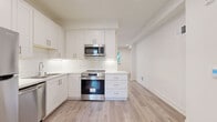 This well-appointed two-floor space showcases a thoughtfully designed interior with a consistent modern aesthetic throughout. The kitchen is a standout feature, outfitted with white shaker-style cabinetry, classic subway tile backsplash, light quartz countertops, and a full suite of stainless steel appliances including a refrigerator, electric range with over-the-range microwave, and dishwasher. Light-toned hardwood flooring runs throughout the main living and kitchen areas, lending warmth and continuity to the open layout. A glass-paneled exterior door in the kitchen area allows natural light to filter in and provides direct outdoor access. The living spaces are bright and neutral, featuring recessed lighting and clean white walls that create an airy, versatile backdrop. Bedrooms are finished with plush carpeting for added comfort, and windows dressed with blinds offer natural light and privacy. The bathroom is a charming detail of the space, featuring a full soaking tub and shower combination, a white vanity with storage, and a striking black-and-white hexagonal tile floor. A staircase connects the two levels, and the overall layout provides a functional flow between all areas. This space presents a fresh, move-in-ready environment with quality finishes throughout.