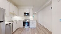 This well-appointed two-floor space showcases a thoughtfully designed interior with a consistent modern aesthetic throughout. The kitchen is a standout feature, outfitted with white shaker-style cabinetry, classic subway tile backsplash, light quartz countertops, and a full suite of stainless steel appliances including a refrigerator, electric range with over-the-range microwave, and dishwasher. Light-toned hardwood flooring runs throughout the main living and kitchen areas, lending warmth and continuity to the open layout. A glass-paneled exterior door in the kitchen area allows natural light to filter in and provides direct outdoor access. The living spaces are bright and neutral, featuring recessed lighting and clean white walls that create an airy, versatile backdrop. Bedrooms are finished with plush carpeting for added comfort, and windows dressed with blinds offer natural light and privacy. The bathroom is a charming detail of the space, featuring a full soaking tub and shower combination, a white vanity with storage, and a striking black-and-white hexagonal tile floor. A staircase connects the two levels, and the overall layout provides a functional flow between all areas. This space presents a fresh, move-in-ready environment with quality finishes throughout.