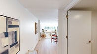 Located at 1 Lyon Pl, Unit 5B in White Plains, NY, this thoughtfully designed one-bedroom, one-bathroom residence offers a clean, modern aesthetic throughout. Light hardwood flooring flows continuously across the entire unit, contributing to a bright and cohesive feel. The open living room is a standout feature, anchored by expansive floor-to-ceiling windows that flood the space with natural light and frame tree-lined views of the surrounding neighborhood. The kitchen is outfitted with contemporary flat-panel cabinetry in a light wood finish, white quartz countertops, a marble-style tile backsplash, and a full suite of stainless steel appliances including a range, over-the-range microwave, and full-size refrigerator. The bedroom is a well-proportioned retreat bathed in natural light, with a wall-mounted split HVAC unit for individual climate control and direct access to outdoor views through a floor-to-ceiling window. The bathroom is finished with striking marble-style wall tile, a wood-toned vanity with an integrated sink, and a clean, modern toilet. A bright entry hallway connects the rooms efficiently, completing this well-appointed and light-filled residence.