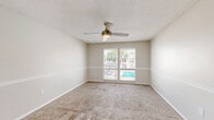 Located at 2100 S Conway Rd in Orlando, FL, this one-bedroom, one-bathroom unit offers a practical and well-organized single-floor layout. The open-concept living and kitchen area serves as the heart of the home, where light wood-look flooring runs throughout. The kitchen features a pass-through counter with granite-look laminate surfaces, white cabinetry, a black refrigerator, and a sink with a tiled backsplash — all visible from the living area, creating a connected and functional space. The living room is finished with plush carpet, a ceiling fan with integrated lighting, and a sliding glass door that leads to an outdoor area, allowing natural light to flow in. A hallway connects the main living space to the bedroom and bathroom. The bedroom is a comfortable, carpeted room equipped with a ceiling fan and double windows that offer pleasant views of a pool and lush outdoor greenery. The bathroom includes a full soaking tub and shower combination with clean white tile surround, a toilet, and wood-look flooring. Throughout the unit, a neutral warm-beige color palette, textured ceilings, and white trim create a clean, cohesive aesthetic.