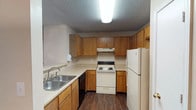 This single-floor residence offers a practical and comfortable layout across several well-defined living spaces. The kitchen is efficiently designed in a U-shaped configuration, featuring warm honey-toned wood cabinetry that extends from floor to ceiling, offering generous storage. Equipped with a white electric range, dishwasher, and refrigerator, the kitchen also includes light-toned countertops and a double stainless steel sink. Dark wood-style flooring runs throughout the kitchen, adding a grounding contrast to the cabinetry. A textured ceiling and overhead fluorescent lighting complete the functional space.

The living area is carpeted and open, highlighted by a ceiling fan with integrated lighting and a tiled fireplace that serves as a natural focal point. A sliding glass door with vertical blinds allows natural light and potential outdoor access. Adjacent to the living space is a dining area with a pendant light fixture and a pass-through to the kitchen, along with an in-unit laundry closet housing a washer and dryer.

The bedrooms are carpeted, with ceiling fans, natural light from windows, and walk-in closets providing notable storage. The bathroom features dark wood-style flooring, a vanity with wood cabinetry, and a full tub-shower combination with white tile surround, offering a clean and straightforward design throughout.