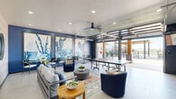 Located at 704 Dale Lane in White Settlement, Texas, this well-appointed community amenity space seamlessly blends indoor comfort with outdoor recreation. The interior lounge area is defined by bold navy blue accent walls adorned with large-scale watercolor cactus murals, creating a lively, Southwestern-inspired atmosphere. Recessed lighting and a ceiling fan maintain comfort throughout, while large glass garage-style doors open fully to the outdoors, allowing natural light to flood the space and creating a fluid indoor-outdoor experience. The lounge is furnished with plush seating arrangements, colorful area rugs, and a full-size ping-pong table, offering a dynamic social environment. A textured geometric accent wall with three circular mirrors adds an additional layer of visual interest. The covered outdoor patio extends the usable space considerably, featuring ceiling fans, comfortable seating, and warm wood-clad columns that contrast with the clean, modern concrete flooring. A separate wood-canopied pergola area provides additional shade and gathering space. The property also includes a resort-style swimming pool outfitted with water fountain features, all enclosed within black iron fencing with views of the surrounding Texas landscape. The overall aesthetic is modern and cohesive, with a consistent navy, white, and natural wood palette throughout.