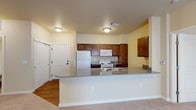 This single-floor 2-bedroom, 2-bathroom residence is designed with a practical and comfortable layout that makes excellent use of its space. The open-concept kitchen and living area serves as the heart of the home, featuring a generous peninsula countertop with grey laminate surfaces that doubles as a breakfast bar. The kitchen is outfitted with rich, warm-toned wood cabinetry, ample storage, and a full suite of white appliances including a refrigerator, range, and built-in microwave. The transition from wood-look flooring in the kitchen to plush carpeting in the living area creates a natural distinction between spaces. The bedrooms are well-proportioned, carpeted for comfort, and include sliding closet doors with vertical blinds that allow for natural light control. The two bathrooms offer distinct configurations: one features a full tub-shower combination with chrome fixtures and wood-look flooring, while the second bathroom includes a separate shower, a wood-toned vanity with an undermount sink, and matching flooring. Warm, neutral wall tones flow throughout the entire residence, creating a cohesive and inviting ambiance. The overall design prioritizes functionality and ease of living across every room.