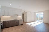 This contemporary single-floor residence showcases a clean, modern design with a thoughtfully open layout. The kitchen and living area flow seamlessly together, creating a bright and airy atmosphere enhanced by abundant natural light streaming through a sliding glass door that leads to an outdoor balcony. The kitchen is well-appointed with a two-tone cabinet scheme, featuring sleek white upper cabinets and dark espresso-toned lower cabinets, all complemented by crisp white countertops. A full suite of stainless steel appliances—including a refrigerator, range, microwave, and dishwasher—adds a polished, functional edge. Recessed lighting illuminates the space throughout.

Light wood-toned flooring runs through the main living areas and bathrooms, providing warmth and continuity across the unit. The bedroom offers a comfortable, carpeted retreat with a sliding-door closet fitted with built-in shelving for ample storage.

Two bathrooms serve the unit: one features a full soaking tub and shower combination with a dark-cabinet vanity, while the second offers a streamlined vanity with a large mirror and modern fixtures. Both bathrooms maintain the unit's consistent clean, white aesthetic with warm wood-toned flooring, creating a cohesive and contemporary feel throughout the entire space.