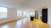 This single-floor unit offers a thoughtfully designed open-concept layout that seamlessly integrates the living area and kitchen. The expansive main living space is finished with light hardwood flooring that extends throughout, lending warmth to the bright, white-walled interior. Large windows along the living area wall allow generous natural light to fill the space.

The kitchen is positioned centrally and features dark espresso cabinetry with granite countertops, a peninsula with pendant lighting overhead, and a full suite of stainless steel appliances including a refrigerator, electric range, microwave, and dishwasher. Track lighting provides additional illumination throughout the open area.

The bedroom is carpeted and bathed in natural light from a pair of corner windows fitted with horizontal blinds. It includes access to a dedicated walk-in closet with a rod system, providing practical storage.

The bathroom is well-appointed with tile flooring, a full tub and shower surround clad in large-format neutral tiles, a dark vanity with a white countertop, and chrome fixtures. The overall design maintains a clean, modern aesthetic throughout.
