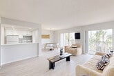 This single-floor, two-bedroom, one-bathroom residence in Fort Lauderdale is designed with a clean, modern aesthetic defined by an all-white palette, light wood-style flooring, and abundant natural light throughout. The open-concept living and dining area forms the heart of the unit, where wide sliding glass doors lead to a private balcony overlooking lush outdoor greenery — a standout feature that draws light deep into the space and enhances its airy feel.

The kitchen is positioned adjacent to the living area behind a white breakfast bar counter, featuring white cabinetry, a tile backsplash, recessed lighting, and white appliances. The dining area sits nearby, bathed in natural light from a window fitted with vertical blinds.

The generously sized primary bedroom offers light wood flooring, a large window, and a dedicated closet with built-in shelving. The second bedroom is well-proportioned with its own window and closet access. The bathroom includes a white vanity with ample drawer storage, a large mirror, a shower-tub combination, and a stacked washer and dryer conveniently located within the unit. Two hallways connect the rooms efficiently, completing this well-organized and bright Fort Lauderdale residence.