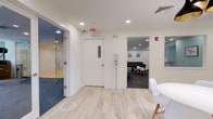 Located at 200 Hopmeadow in Weatogue, Connecticut, this single-floor amenity center offers a comprehensive range of fitness and community spaces designed with a clean, modern aesthetic. The facility is anchored by a spacious main fitness area outfitted with treadmills, ellipticals, a weight bench, and large windows that invite natural light and outdoor views. An adjacent strength and free weights room features floor-to-ceiling mirrors, wall-mounted TVs, a full dumbbell rack, medicine balls, and cable machines, all set on durable rubber flooring. A dedicated spin studio accommodates multiple cycling bikes and is accented by a dramatic landscape mural and a window overlooking the grounds. A light-wood-floored movement and yoga studio with glass partition walls provides an open, versatile space for group classes or personal training. The community spaces include a stylish conference room with a sleek black table, leather chairs, and natural light, ideal for meetings or events. A welcoming lobby area features light hardwood flooring, a stainless steel elevator, curated wall art, and casual seating. A children's play room with a wall-mounted TV, soft seating, and activity table rounds out the offerings, making this a well-appointed, multi-purpose facility suited for residents and professionals alike.
