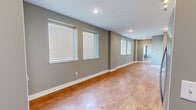 This efficiently designed single-floor unit offers a thoughtful layout across one bedroom, one bathroom, and a combined kitchen and living area. Warm hardwood-style flooring runs consistently throughout the space, complementing the neutral taupe and gray wall tones that create a clean, cohesive aesthetic.

The open living area is notably elongated, lined with multiple windows dressed in white horizontal blinds that invite ample natural light. Recessed ceiling lighting provides additional illumination, enhancing the bright and airy feel of the room.

The kitchen is well-equipped with a full suite of stainless steel appliances, including a refrigerator with ice and water dispenser, electric range, built-in microwave, and dishwasher. Crisp white shaker-style cabinetry extends to the ceiling for generous storage, while gray countertops and a stainless steel sink complete the functional and modern design.

The bedroom offers a comfortable footprint with two windows for natural light and includes a closet with built-in shelving and hanging rods. The bathroom features a tiled tub-shower combination with a decorative mosaic accent border, a light blue shaker-style vanity with a white countertop, a large mirror, and marble-style tile flooring, lending a clean and polished finish to the space.