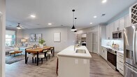 Located at 100 Waddell Plaza Ln in Cary, NC, this well-appointed 2-bedroom, 2-bathroom residence offers a thoughtfully designed single-floor layout with a cohesive, modern aesthetic. The open-concept living, dining, and kitchen area serves as the heart of the home, bathed in natural light from large windows that frame views of the surrounding community. The living room features wood-look flooring, a ceiling fan, and direct access to an outdoor balcony. The kitchen is equipped with stainless steel appliances, soft gray cabinetry, a built-in wine rack, pendant lighting, and a generous white quartz island with bar seating — ideal for both cooking and entertaining. The spacious primary bedroom provides a serene retreat with warm neutral tones, hardwood-style flooring, and a ceiling fan. Its en-suite bathroom showcases a dual-sink vanity with white quartz countertops, black hardware accents, wood-framed mirrors, and a floor-to-ceiling marble-tiled walk-in shower. The second bathroom mirrors this refined design. Both bedrooms are complemented by well-organized walk-in closets with built-in shelving and hanging storage. Neutral wall tones, clean architectural lines, and wood-look flooring create a warm yet contemporary ambiance throughout the entire residence.