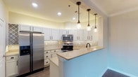 Unit 306 is a thoughtfully designed single-floor residence that combines modern finishes with functional layout. The kitchen serves as a standout feature, showcasing white shaker cabinetry with matte black hardware, granite countertops, and a striking chevron-patterned tile backsplash. Stainless steel appliances, including a range, microwave, and refrigerator, complement the space, while a peninsula with pendant lighting provides additional prep and seating space. A white undermount sink with a matte black faucet adds a refined contrast.

The living and dining areas are defined by rich, dark hardwood-style flooring, crown molding, and neutral warm-toned walls. Arched architectural details and built-in shelving add character throughout. A glass-paned door leads to a private balcony, allowing natural light to filter into the living space.

The bedrooms are finished with plush carpet flooring, providing a comfortable retreat. Two bathrooms serve the unit: one featuring a soaking tub and wood-style flooring, and the other equipped with a walk-in shower and a wide granite vanity countertop with a square vessel-style sink. Both bathrooms feature matte black hardware accents, maintaining a cohesive aesthetic throughout the residence.