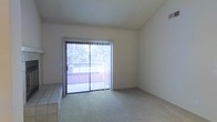 This single-floor residence offers a clean, functional layout with neutral finishes throughout. The living area is a standout feature, characterized by light-toned carpet flooring that transitions to tile near the entryway or adjacent spaces, creating a natural delineation between zones. A large sliding glass door floods the room with natural light and provides direct access to an outdoor balcony, where lush greenery is visible beyond the railing — offering a pleasant connection to the outdoors. Vertical blinds on the sliding door allow for flexible light control and privacy. The walls are finished in a soft, neutral white, complementing the textured ceiling and contributing to a bright, open atmosphere. The overall ambiance of the space is calm and understated, providing a versatile canvas well-suited for a variety of interior styles. The single-floor configuration ensures easy accessibility and a seamless flow throughout the home, making it a practical and comfortable living environment.