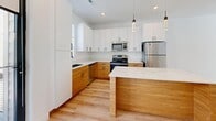 This well-appointed multi-story residence spans three floors and offers a thoughtfully designed layout with 2 bedrooms and 3 full bathrooms. The main living floor serves as the heart of the home, featuring an open-concept kitchen and living area that showcases a striking two-tone cabinetry design — warm natural wood lower cabinets paired with sleek white upper cabinets and quartz countertops. A kitchen island provides additional prep and gathering space, while stainless steel appliances, a undermount sink, and modern pendant lighting complete the culinary space. Light wood flooring flows throughout the main level, complemented by an abundance of natural light from large windows and access to an outdoor balcony. The upper floor houses the bedrooms, each carpeted for comfort and featuring generous windows that frame outdoor greenery and hillside views. The primary bedroom offers a spacious layout with high ceilings and its own access to a bathroom. The secondary bedroom includes a built-in closet with double doors. Each of the three bathrooms is finished consistently with wood-toned vanities, quartz countertops, and clean white tub-shower combinations set on light wood-look flooring. The overall aesthetic throughout is clean, modern, and bright, creating a cohesive and move-in-ready living environment.