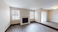 This single-story 2-bedroom, 2-bathroom residence in Memphis, Tennessee offers a well-organized layout with a comfortable mix of wood-look vinyl flooring and plush carpet throughout. The living room serves as the heart of the home, anchored by a classic white-mantled fireplace with tile surround and flanked by multiple windows that fill the space with natural light. The living area flows into an adjacent dining space, with a sliding glass door opening to an outdoor patio view. The kitchen is efficiently designed with warm wood cabinetry, a decorative tile backsplash, and a full suite of black appliances including a refrigerator, electric range, and over-the-range microwave. Both bedrooms are carpeted and well-proportioned, each featuring windows that bring in natural light. One bedroom includes access to a walk-in closet area. A central hallway connects the bedrooms to both bathrooms. The bathrooms feature warm wood vanity cabinetry with large mirrors, and one includes a tiled shower-tub combination with wood-look flooring. Neutral tones are used throughout the home, creating a clean and cohesive aesthetic.