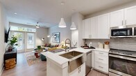 This single-floor residence offers a thoughtfully designed open-concept layout that seamlessly connects the kitchen, dining, and living areas. The kitchen is a standout feature, outfitted with white shaker cabinetry, a grey subway tile backsplash, stainless steel appliances including a refrigerator, range, microwave, and dishwasher, and a central island with a deep stainless steel sink and pendant lighting overhead. Light wood-tone flooring runs throughout, lending a clean, cohesive aesthetic to the space.

The living area is bright and inviting, benefiting from natural light through large windows and a set of French doors that open to an exterior balcony. A ceiling fan adds comfort, and the neutral wall tones create a versatile backdrop for a range of furnishing styles.

The bedroom is a calm retreat with a large window that brings in natural light and offers views of the surrounding area. It connects directly to a full bathroom featuring white cabinetry, a framed mirror, and a tub-shower combination. Adjacent to the bathroom is a generously sized walk-in closet with built-in shelving and hanging rods, providing ample storage.

A hallway near the entry houses a stacked in-unit washer and dryer, adding everyday convenience. The entry area also features a built-in bench nook, completing this well-organized and modern residence.
