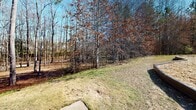 Located in Columbus, Georgia (31904), this single-level outdoor community space offers a welcoming environment surrounded by natural beauty. The grounds are characterized by gently sloping grassy areas that transition into a backdrop of tall pines and mixed deciduous trees, providing a natural buffer and a sense of privacy throughout the property.

A standout feature of this space is the dedicated playground area, equipped with a multi-level play structure complete with slides, a covered tower, and interactive elements, all set within a wood chip safety surface bordered by timber edging. This makes the area well-suited for families with children.

Concrete walkways wind through the property, providing smooth and accessible pathways connecting the various areas of the community. The well-maintained grounds include open lawn spaces that offer room for outdoor activities and relaxation. Neighboring residential buildings are visible in the background, reinforcing the community-oriented character of the space.

The mature tree line along the perimeter not only adds to the aesthetic appeal but also provides natural shade and a serene, park-like ambiance. Under clear blue skies, the combination of open green space, wooded edges, and community amenities creates an inviting outdoor environment for residents of this Columbus, GA neighborhood.