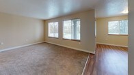 This single-floor unit offers a practical and comfortable layout designed for everyday living. The spacious living area is bathed in natural light through a large bank of windows fitted with blinds, and features plush neutral carpeting that creates a warm, inviting atmosphere. A pass-through window connects the living space to the kitchen, maintaining an open feel between the two areas. The kitchen is well-equipped with stainless steel appliances, including a refrigerator and gas range, complemented by white cabinetry with wood-toned accents, a built-in sink, and durable wood-style flooring that extends throughout the kitchen and entry areas. The bedrooms are generously sized, each carpeted and featuring windows with blinds that allow for ample natural light and views of the surrounding neighborhood. The full bathroom is thoughtfully finished with a wide vanity offering cabinet storage, a single sink, a toilet, and a full-size soaking tub with a shower, all set on clean wood-style flooring. The unit's neutral color palette of warm beige tones throughout creates a cohesive and move-in-ready aesthetic, while textured ceilings add a subtle architectural detail. The layout flows efficiently from room to room, making this a functional and comfortable living space.