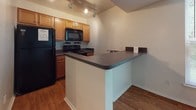 Located at 99 Crater Cir in Petersburg, Virginia, this single-floor residence offers a practical and well-organized layout. The living area features warm hardwood-style flooring and neutral white walls that create a bright, clean atmosphere, with a window allowing natural light to fill the space. A central hallway connects the main rooms, lined with closet storage and finished with consistent hardwood-style flooring throughout.

The kitchen is efficiently designed with warm wood cabinetry, dark granite-style countertops, and black appliances including a range, microwave, and refrigerator. Track lighting overhead illuminates the workspace, and a peninsula counter with additional countertop space provides a convenient area for casual dining or meal preparation. A stainless steel sink completes the functional layout.

The bedroom is carpeted for comfort, features a large window for natural light, and includes a double-door closet for ample storage. The bathroom is clean and straightforward, offering a full tub-shower combination and a vanity mirror.

A notable convenience of this residence is the in-unit stacked washer and dryer, situated just off the bathroom — a practical feature that adds everyday ease. Overall, the space presents a functional and comfortable single-floor living environment with consistent finishes throughout.