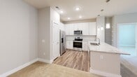 Located at 6440 Carrara Pl in Charlotte, NC, this well-appointed 2-bedroom, 2-bathroom residence offers a thoughtfully designed single-floor layout with a clean, modern aesthetic throughout. The open-concept kitchen serves as the heart of the home, showcasing white shaker cabinetry, a classic subway tile backsplash, granite countertops, stainless steel appliances, and stylish pendant lighting over a peninsula with additional built-in shelving nearby — ideal for storage and display. Wood-look flooring runs through the kitchen and bathrooms, while plush carpeting lines the living areas and bedrooms for added comfort. The generously sized primary bedroom features multiple windows framing lush tree views, a ceiling fan, and direct access to an en suite bathroom complete with a glass-enclosed shower, granite vanity, and a walk-in closet with built-in shelving. The second bedroom is equally bright, with its own ceiling fan and a large window overlooking greenery. The second bathroom offers a full tub-shower combination and a matching granite vanity. A dedicated laundry room houses a full-size Whirlpool washer and dryer. Neutral tones and abundant natural light create a calm, inviting atmosphere throughout this Charlotte residence.
