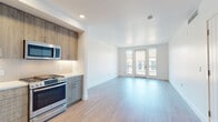 Located at 1258 El Camino Real in Menlo Park, California, this thoughtfully designed single-floor residence offers a clean, contemporary aesthetic throughout. The open-concept living and kitchen area is anchored by light wood-tone flooring that flows seamlessly across the entire space, creating a bright and cohesive feel. Large French doors lead to a private balcony, flooding the living area with natural light and providing outdoor views of the surrounding neighborhood.

The kitchen is well-appointed with two-tone wood cabinetry—warm upper cabinets complemented by cooler gray lower units—set against a white tile backsplash and light quartz countertops. Stainless steel appliances include a gas range, over-the-range microwave, and a French door refrigerator, offering a fully equipped cooking space.

The bedroom features its own set of French doors opening to a balcony, along with a dedicated walk-in closet outfitted with built-in shelving and hanging rods for organized storage. The bathroom is finished with mosaic tile flooring, a combination tub and shower, a wood-grain vanity with a white countertop, and a backlit mirror, delivering a clean and modern aesthetic. Recessed lighting and white walls throughout contribute to the space's bright, airy ambiance.