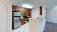 This two-floor space is designed with practicality and comfort in mind. The kitchen is well-appointed, featuring warm medium-toned wood cabinetry with sleek hardware, stainless steel appliances including a gas range, over-the-range microwave, and refrigerator, complemented by light countertops and a peninsula with a built-in sink. Light tile flooring runs throughout the kitchen, enhancing its clean, functional aesthetic.

The living area is notably spacious, highlighted by soaring vaulted ceilings that lend an open, airy atmosphere. Neutral-toned carpet covers the floor, adding warmth to the expansive room. A ceiling fan is installed overhead, contributing to year-round comfort.

The bedrooms are finished with the same neutral carpet and feature bright white walls. At least one bedroom offers access to a dedicated walk-in closet equipped with built-in shelving, providing ample storage. Additional bedrooms include windows fitted with blinds, allowing for natural light while maintaining privacy.

The bathroom is clean and efficiently laid out, featuring a tiled tub-shower combination, a toilet, and light tile flooring. The overall palette throughout the space is neutral and understated, creating a versatile backdrop suited to a variety of interior styles.