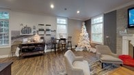 Located at 100 Mariners Cir in Sheffield Lake, Ohio, this single-floor gathering space is thoughtfully designed to serve as a versatile community hub. The open layout seamlessly connects multiple functional zones, creating an inviting atmosphere throughout.

The kitchenette area is appointed with rich cherry wood cabinetry, dark countertops, and a deep blue accent wall that adds a bold, stylish contrast. A beverage cooler, microwave, and sink make the space well-equipped for entertaining. Tile flooring grounds this zone and transitions into warm hardwood-style flooring across the rest of the space.

The lounge area serves as the heart of the room, centered around a classic fireplace with a white mantel and a stone surround accent wall. Large windows on multiple sides flood the space with natural light and offer views of the surrounding greenery.

A billiards and bar area provides a social focal point, featuring high-top tables with industrial-style seating and a pool table, all framed by crown molding and recessed lighting. An adjacent workspace or consultation area includes a desk, display boards, and a bistro-style table, making it suitable for meetings or resident services. The overall ambiance is warm, modern, and welcoming throughout.