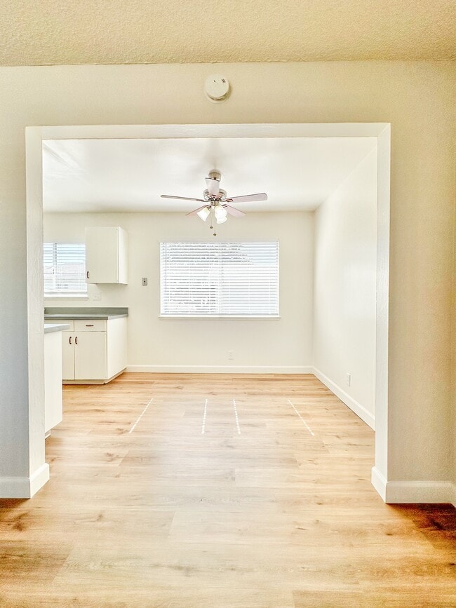 an empty living room with a ceiling fan and a kitchen - Gallatin Apartments
