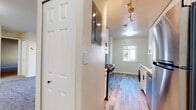 This single-floor residence offers a thoughtfully organized layout across several distinct living areas. The galley-style kitchen is a functional highlight, featuring stainless steel appliances including a gas range, over-the-range microwave, and dishwasher. White shaker-style cabinetry pairs cleanly with granite countertops, while light wood-look flooring runs throughout the kitchen and entry corridor. Track lighting overhead adds a modern touch, and a window at the end of the kitchen draws in natural light.

The living area is carpeted and generously proportioned, with neutral walls and a sliding glass door that opens to a balcony, offering outdoor views and additional natural light. The transition between the living space and adjoining rooms is defined by clean architectural framing.

The bedrooms are carpeted with neutral tones and include closet storage. One bedroom features two closets and connects to additional rooms, while another is well-lit by a window overlooking the exterior.

The bathroom is neatly appointed with a white vanity, light countertop surface, black hardware accents, a large mirror, and a tub-shower combination, all set on wood-look flooring. Throughout the space, a consistent palette of warm neutrals and white trim creates a clean, cohesive ambiance.