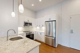 This well-designed one-bedroom, one-bathroom residence in Natick, MA offers a thoughtfully organized layout across a single floor. The open-concept living area seamlessly connects the kitchen, dining, and living spaces, creating an inviting and functional environment. The kitchen is a standout feature, equipped with crisp white shaker cabinetry, a striking granite-topped island with an undermount sink and integrated dishwasher, full stainless steel appliances including a French door refrigerator, over-range microwave, and electric range, all accented by a classic subway tile backsplash and elegant pendant lighting. Warm hardwood-style flooring flows throughout the main living areas, adding a sense of continuity and warmth. The bedroom offers plush carpeting, a large window with outdoor views, and access to a closet, providing a comfortable and private retreat. The bathroom is finished with modern tile flooring, a glass-enclosed walk-in shower with tiled walls, a white shaker vanity with a clean white countertop, and a well-lit mirror. Additional conveniences include in-unit laundry and two closets for ample storage. The space features tall ceilings and recessed lighting throughout, contributing to its bright and airy ambiance.