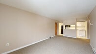 Located at 1700 Western Ave in Albany, NY, this one-bedroom, one-bathroom residence offers a thoughtfully organized floor plan that makes efficient use of its space. The living room is open and inviting, featuring neutral beige walls, wall-to-wall carpet, and a baseboard heating system. A large sliding glass door with red-framed accents allows generous natural light to fill the room while offering outdoor views of the surrounding neighborhood. The living area flows seamlessly toward the kitchen, which is accessible via an open pass-through counter. The kitchen is well-equipped with white cabinetry, granite-patterned countertops, a stainless steel sink, a white electric range, a black refrigerator, and an overhead microwave. White tile flooring and a drop ceiling complete the kitchen's clean, functional aesthetic. The spacious bedroom features the same neutral carpeting and warm-toned walls, with large windows providing additional natural light and views. A dedicated closet with built-in storage and warm wood-toned sliding doors adds practicality. The bathroom includes a full tub and shower combo with built-in shelving, a vanity with mirror, and classic white tile flooring. A hallway and additional closet round out this well-appointed residence.