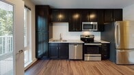 Located at 19 Dowling Village Blvd in North Smithfield, Rhode Island, this single-floor residence offers a thoughtfully designed layout with modern finishes throughout. Rich hardwood flooring flows seamlessly across the open-concept living and kitchen areas, creating a warm and cohesive aesthetic. The kitchen is a standout feature, equipped with dark espresso cabinetry reaching to the ceiling for ample storage, light granite countertops, and a full suite of stainless steel appliances including a range, dishwasher, and microwave. Recessed lighting illuminates the combined living and dining area, which offers generous open space and connects naturally to the rest of the home. A private balcony is accessible through a glass-paneled door, flanked by windows that draw in abundant natural light and provide pleasant views of surrounding greenery. The bathroom is finished with classic black-and-white mosaic tile flooring, dark vanity cabinetry, and clean white walls, offering a timeless and crisp look. A barn-style sliding door adds a contemporary touch to the interior hallway. The overall ambiance is bright, clean, and modern, making this a comfortable and stylish space in a convenient Rhode Island location.