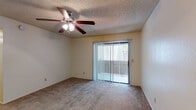 Located at 7351 E Speedway Blvd in Tucson, Arizona, this single-floor residence offers a practical and comfortable layout designed for everyday living. The living area is generously sized, featuring neutral-toned carpet, a ceiling fan with built-in light fixture, a textured ceiling, and a sliding glass door fitted with vertical blinds that opens to an outdoor patio, allowing natural light to fill the space. The entry transitions from hardwood-style flooring near the front door to soft carpet throughout the main living zones. The galley-style kitchen is efficiently organized with wood-toned cabinetry, laminate countertops, hardwood-style flooring, and a full suite of white appliances including a refrigerator, electric range, and dishwasher, all topped by an overhead ventilation hood. The bedroom features carpeted flooring, a window with blinds for natural light, and direct access to a walk-in closet as well as an en suite bathroom. The en suite bath includes a single vanity with wood cabinetry, a large mirror, and a separate shower stall. A second bathroom offers a full tub-shower combo with white tile surround and hardwood-style flooring. An additional carpeted room with a textured ceiling provides flexible use as a second bedroom or office.