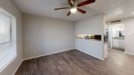 Located at 1839 S Glenbrook Dr in Garland, TX, this single-floor unit offers an efficient and well-organized layout that makes thoughtful use of its compact footprint. The living and dining area share an open, combined space anchored by rich, dark hardwood-style flooring and neutral gray walls that lend a clean, modern feel. A ceiling fan with a built-in light fixture provides both air circulation and ambient lighting. A pass-through counter connects the living/dining area to the kitchen, creating a sense of openness between the two spaces. The kitchen is equipped with white cabinetry, granite-look countertops, a stainless steel sink, and black appliances including a full-size refrigerator and dishwasher. The textured ceilings are consistent throughout the unit. Two bathrooms serve the space, each featuring granite-look vanity countertops, white cabinetry, and wood-style flooring. The full bathroom includes a tiled tub-and-shower combination with large-format white tile. A dedicated closet provides additional storage. Natural light enters through a window near the front entrance, which features a solid white panel door. Overall, the unit presents a straightforward, functional design with consistent finishes throughout.