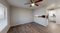 Located at 1839 S Glenbrook Dr in Garland, TX, this single-floor unit offers an efficient and well-organized layout that makes thoughtful use of its compact footprint. The living and dining area share an open, combined space anchored by rich, dark hardwood-style flooring and neutral gray walls that lend a clean, modern feel. A ceiling fan with a built-in light fixture provides both air circulation and ambient lighting. A pass-through counter connects the living/dining area to the kitchen, creating a sense of openness between the two spaces. The kitchen is equipped with white cabinetry, granite-look countertops, a stainless steel sink, and black appliances including a full-size refrigerator and dishwasher. The textured ceilings are consistent throughout the unit. Two bathrooms serve the space, each featuring granite-look vanity countertops, white cabinetry, and wood-style flooring. The full bathroom includes a tiled tub-and-shower combination with large-format white tile. A dedicated closet provides additional storage. Natural light enters through a window near the front entrance, which features a solid white panel door. Overall, the unit presents a straightforward, functional design with consistent finishes throughout.
