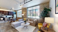 Located at 144 4th St in Burlington, NC, this two-bedroom, two-bathroom loft showcases an impressive industrial-chic aesthetic throughout. The open-concept living and kitchen area is the heart of the space, defined by dramatic exposed brick walls, soaring ceilings with visible ductwork, and oversized steel-framed windows that flood the interior with abundant natural light and outdoor views. Polished concrete-style floors run throughout, adding to the loft's raw, urban character.

The kitchen is well-appointed with rich dark-wood cabinetry, granite countertops, stainless steel appliances including a refrigerator, range, microwave, and dishwasher, and a double-basin sink — all complemented by a built-in wine rack overhead. A dining area sits adjacent, with direct sightlines to the brick accent wall and oversized windows.

The primary bedroom offers a calm, neutral retreat with a ceiling fan and clerestory window for added light. The second bedroom functions well as a flexible workspace or guest room, featuring high ceilings and ample floor space. Both bathrooms are clean and functional, with tub-shower combinations. Hallways and a dedicated closet complete the efficiently designed floor plan, making this a well-rounded urban residence.