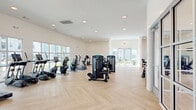 Located at 49 N Assembly Dr in Wilmington, NC, this modern fitness center spans a generous single floor, offering a thoughtfully designed environment for a comprehensive workout experience. The space is divided into two distinct areas: a main gym floor and a separate studio room, both unified by a striking light-toned herringbone hardwood floor that adds warmth and visual interest throughout.

The main gym area is bright and open, featuring high ceilings, recessed lighting, and expansive windows along multiple walls that flood the space with natural light and provide views of the surrounding community. The room is well-appointed with a full suite of True-brand strength machines, cable systems, treadmills, ellipticals, stationary bikes, and a dedicated dumbbell rack. A wall-mounted flat-screen TV adds convenience for users during workouts.

The adjacent studio room offers a more versatile, open-plan layout beneath a warm wood-paneled ceiling with recessed lighting. A full-panel glass garage door opens to the outdoors, allowing fresh air and additional light to flow in. The studio is stocked with yoga mats, stability balls, resistance equipment, and other group fitness accessories, making it ideal for stretching, yoga, or guided classes. Together, the two areas create a complete, modern fitness facility suited for a wide range of exercise routines.