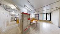 Located at 35 David Salomon Drive in Toronto, this shared laundry facility offers a well-organized, functional space designed to accommodate the needs of multiple residents. The room is generously sized, with a bright, open layout illuminated by fluorescent tube lighting mounted to the ceiling alongside exposed conduit runs that give the space a utilitarian character.

The laundry area is equipped with multiple top-loading washing machines and front-loading dryers arranged in orderly rows, providing ample capacity for simultaneous use. A long continuous countertop runs along one wall, offering convenient folding and sorting space, complemented by a sturdy wooden work table positioned in the open floor area. Neutral beige ceramic wall tiles line the lower portions of the walls, while the upper walls are finished in white, contributing to a clean and practical aesthetic.

The durable terrazzo flooring throughout the space is easy to maintain and well-suited for high-traffic use. Natural light filters in through frosted windows, supplementing the overhead lighting. Additional features include a Canada Post parcel locker station for resident convenience, clearly marked emergency exits, and ceiling-mounted security cameras. A secondary access door connects to an adjoining corridor, ensuring smooth flow in and out of the facility. Overall, the space is thoughtfully arranged to deliver an efficient shared laundry experience.