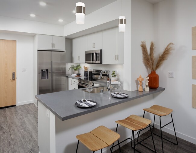 model kitchen with a large island with two stools and a stainless steel refrigerator - Esperanza at Duarte Station