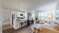 Located in Somerset Park in Leesburg, VA, this one-bedroom, one-bathroom residence offers a thoughtfully designed open-concept layout finished with wood-style flooring and crown molding throughout the main living areas. The kitchen is a standout feature, showcasing white shaker cabinetry, granite countertops, stainless steel appliances including a gas range and built-in microwave, and a peninsula with bar seating — ideal for casual dining or entertaining. A dedicated dining area sits adjacent, bathed in natural light from a large window with blinds. The living room is bright and inviting, with generous window coverage that brings in abundant natural light and views of the surrounding greenery. The bedroom offers plush carpeting, crown molding, and a window that continues the home's light-filled character. The full bathroom is well-equipped with a granite vanity, tub-shower combination with subway tile surround, and tile flooring. Two closets provide ample storage throughout, and a dedicated laundry area houses a stacked full-size washer and dryer. The overall ambiance is clean, modern, and comfortable — a refined living space in a serene Virginia community.