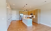 This 820-square-foot, one-bedroom, one-bathroom unit at 4362 Watermark Dr in Wilmington, NC offers a thoughtfully designed open-concept floor plan with modern finishes throughout. The combined kitchen and living area serves as the heart of the home, featuring light wood cabinetry extending to the ceiling, white quartz countertops, a subway tile backsplash, and stainless steel appliances including a French door refrigerator, electric range, and built-in microwave. A large central island with pendant lighting adds both functionality and style, while light wood-look flooring ties the space together. The living area benefits from an expansive bank of windows and a ceiling fan, filling the room with natural light and outdoor views. The 170-square-foot bedroom is carpeted, includes a ceiling fan, and connects directly to a walk-in closet outfitted with dual hanging rods and shelving. The bathroom features a sleek walk-in shower with a frameless sliding glass door and matte black hardware. A private balcony with modern metal grid railings completes the unit, offering open sky views over the surrounding landscape.