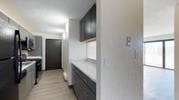 This single-floor residence offers three bedrooms and one and a half bathrooms, thoughtfully laid out to maximize functionality and comfort. The kitchen is a standout feature, showcasing contemporary dark cabinetry with sleek hardware, complemented by crisp marble-style countertops that lend a clean, modern aesthetic. Upper and lower cabinets provide ample storage, while a window above the counter allows natural light to brighten the workspace. The flooring throughout features light-toned wood-look planks that add warmth and continuity to the space. A well-lit entry corridor connects the kitchen area to the front entrance, which is fitted with a solid security door, contributing to both safety and a polished look. Textured walls add character and depth throughout the interior. The pendant lighting in the hallway provides a subtle decorative touch while ensuring the space remains well-lit. With three bedrooms, this residence offers flexibility for families, roommates, or those in need of dedicated office or guest space. The half bathroom adds convenience for guests, while the full bathroom serves the main living quarters. Overall, the space combines practical design with modern finishes, creating a welcoming and well-appointed home environment.