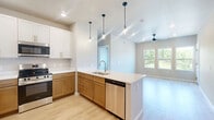 This well-appointed 2-bedroom, 2-bathroom unit at 5176 Old Town Hall Rd in Eau Claire, WI offers a thoughtfully designed single-floor layout. The kitchen is a standout feature, showcasing two-tone cabinetry with white upper cabinets and warm wood lower cabinets, stainless steel appliances including a refrigerator, range, and microwave, light quartz countertops, a undermount sink, and pendant lighting that adds a modern touch. Light wood-tone flooring flows seamlessly throughout the living areas and bedrooms, creating a bright and cohesive aesthetic. The combined kitchen and living room area provides an open, functional space ideal for everyday living. Both bedrooms are comfortably sized, equipped with ceiling fans, and feature windows that frame lush green outdoor views, filling each room with natural light. The primary bedroom includes access to a closet. Both bathrooms are finished with warm wood vanities, white countertops, framed mirrors, gold-toned hardware and grab bars, and neutral tile flooring, offering a clean and contemporary feel. The unit's neutral color palette throughout lends a calm, move-in-ready ambiance, while multiple windows across the unit provide panoramic views of the surrounding green landscape.