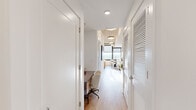 This contemporary high-rise residence offers a thoughtfully designed single-floor layout that blends modern aesthetics with functional living. Light hardwood flooring flows throughout, connecting each space seamlessly from entry to living area.

The open-concept living and dining area is anchored by floor-to-ceiling windows that frame sweeping panoramic city and treetop views, flooding the interior with abundant natural light. Exposed ductwork on the ceiling adds an industrial loft character, complementing the clean white walls and modern furnishings.

The galley-style kitchen is well-equipped with warm wood upper cabinetry, white lower cabinets, light stone countertops, a white tile backsplash, and a full suite of stainless steel appliances including a dishwasher, microwave, and refrigerator.

A long corridor leads to the private quarters, lined with clean white doors and recessed lighting overhead. The bedroom features crisp white walls, decorative wall sconces, and a warm, curated aesthetic with mid-century inspired nightstands.

The bathroom is accessed off the hallway and features a wood-toned vanity with ample drawer storage, a clean tile floor, and a large mirror — offering a calm, spa-like feel. Throughout the residence, the interplay of natural light, elevated city views, and carefully selected finishes creates a polished and inviting urban living environment.
