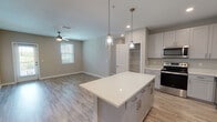 This single-floor residence showcases a thoughtfully designed open-concept layout that seamlessly connects the kitchen and living areas. The kitchen serves as the centerpiece of the space, anchored by a generously sized island with a sparkling quartz countertop and pendant lighting overhead. White shaker-style cabinetry with brushed nickel hardware lines the walls, complemented by a full suite of stainless steel appliances, including a range, microwave, dishwasher, and French door refrigerator. A deep undermount sink with a modern faucet completes the workspace. Built-in shelving near the kitchen entrance provides additional storage and display space.

The adjoining living area features light wood-style flooring that carries throughout the main living spaces, neutral gray-toned walls, recessed lighting, and a ceiling fan. Natural light filters in through multiple windows with blinds, and a door provides access to an outdoor area. The open layout creates a comfortable, connected atmosphere ideal for everyday living and entertaining.

The bedrooms feature plush carpeting, neutral walls, and ceiling fans. One bedroom offers dual windows that bring in abundant natural light and views of the surrounding neighborhood. The overall aesthetic is clean, modern, and move-in ready.