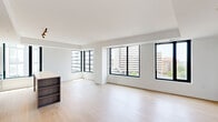 This well-appointed unit offers a thoughtfully designed single-floor layout accommodating two bedrooms and two full bathrooms. The open-concept living and dining area immediately impresses with its expansive floor plan, light hardwood flooring, and large black-framed windows that frame panoramic city views, filling the space with abundant natural light.

The kitchen is a standout feature, boasting a contemporary design with two-tone cabinetry — combining dark wood lower cabinets with crisp white upper cabinets — complemented by stainless steel appliances including a refrigerator, range, and built-in microwave. A sizeable kitchen island with a light stone countertop provides additional workspace and casual seating, while a large window offers continued city views.

The primary bedroom is a comfortable, well-lit retreat featuring hardwood floors and a large window with a balcony view. The second bedroom similarly benefits from generous natural light through a wide, black-framed window. Both bathrooms maintain the unit's clean aesthetic, with one featuring a full soaking tub with white subway tile surround and neutral stone-tiled flooring. Two hallways connect the spaces efficiently, contributing to the unit's logical and functional flow throughout.