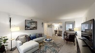 Located at 35 Goldsmith Pl in Newport News, Virginia, this single-floor residence offers a well-organized layout designed for comfortable everyday living. The open living room is generously proportioned, featuring soft carpeting, neutral walls, and a large front-facing window that allows natural light to fill the space. The room easily accommodates a full sectional seating arrangement alongside additional accent chairs, creating a versatile and inviting atmosphere. Adjacent to the living area, a dedicated dining room features a tray ceiling with a ceiling fan and provides a defined, intimate setting ideal for meals and entertaining. The kitchen is efficiently designed with warm wood cabinetry, dark granite-style countertops, wood-look vinyl flooring, and black appliances including an electric range, dishwasher, and refrigerator, offering ample storage and counter space. The primary bedroom is a serene retreat with plush carpeting, a large window for natural light, and generous closet space. A second bedroom provides equal comfort, also carpeted and naturally lit, suitable for use as a guest room or home office. Throughout the residence, the clean white walls and consistent flooring choices create a cohesive and functional living environment.