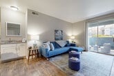 This single-floor residence offers a thoughtfully designed layout that balances comfort and functionality across its living spaces. The living room serves as the heart of the home, featuring warm wood-style flooring, neutral gray walls, and a sliding glass door that opens to a private outdoor patio, flooding the space with natural light and offering pleasant exterior views. Adjacent to the living area, a dedicated dining space accommodates a round glass-top table and provides a refined yet casual setting for meals.

The kitchen is outfitted with stainless steel appliances, including a refrigerator, range, and dishwasher, complemented by white cabinetry, granite-style countertops, and a classic subway tile backsplash. Wood-style flooring continues through the kitchen, maintaining a cohesive aesthetic.

The primary bedroom is generously proportioned, featuring plush carpeting, multiple windows that invite ample natural light, and a ceiling fan for year-round comfort. A second bedroom offers similar finishes and versatile utility. The bathroom is cleanly finished with wood-look flooring and straightforward fixtures.

Throughout the residence, a consistent neutral color palette and mid-century modern styling create a cohesive, inviting ambiance well-suited for everyday living.