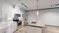 Located at 12501 Honore Ave in Sarasota, FL, this well-appointed one-bedroom, one-bathroom residence offers a thoughtfully designed open-concept layout. Wood-look flooring flows throughout the main living areas, creating a warm, cohesive aesthetic.

The combined kitchen, dining, and living area serves as the heart of the home. The kitchen stands out with sleek white cabinetry featuring a marble-inspired finish, granite countertops, a center island with an undermount sink, stainless steel appliances including a French door refrigerator and electric range, and stylish pendant and track lighting overhead.

The living and dining area is bright and open, accented by dark crown molding and windows that invite natural light. A patio extends the living space outdoors, offering views of the surrounding greenery.

The bedroom is a comfortable retreat finished with plush carpeting, a ceiling fan, and a window overlooking lush palm-lined scenery. Three closets provide generous storage throughout the unit.

The bathroom features dual vessel sinks set in a granite vanity with wood-toned cabinetry, a large mirror, and hardwood-style flooring, with a walk-in shower visible beyond. In-unit laundry and a dedicated hallway complete this functional and modern Sarasota residence.