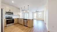 This thoughtfully designed single-story residence offers 1 bedroom and 2 full bathrooms within a well-appointed, open-concept floor plan. Light hardwood flooring flows seamlessly throughout every room, creating a cohesive and airy atmosphere.

The kitchen serves as a central hub, featuring a two-tone cabinet design with white upper cabinets and natural wood lower cabinets, granite countertops, a peninsula with pendant lighting overhead, and a full suite of stainless steel appliances including a refrigerator, range, microwave, and dishwasher. The kitchen opens directly into the living area, which benefits from abundant natural light through large windows and a glass door leading to the outdoors, further enhanced by a ceiling fan above.

The primary bedroom is a comfortable retreat with windows framing greenery outside and a dedicated ceiling fan. It connects to a spacious walk-in closet with built-in shelving on both sides, providing generous storage. The en-suite primary bathroom features a granite-topped vanity with white cabinetry, black hardware accents, a large mirror, and a glass-enclosed walk-in shower. The second full bathroom mirrors the same refined aesthetic with a granite vanity, white cabinetry, and a tub-shower combination. Two closets throughout the unit offer additional storage flexibility.